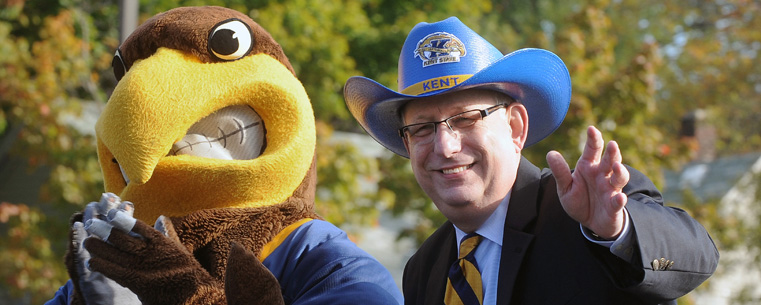 <p>Flash, Kent State's mascot, waves to spectators along the Homecoming parade route along with Kent State President Lester A. Lefton.</p>