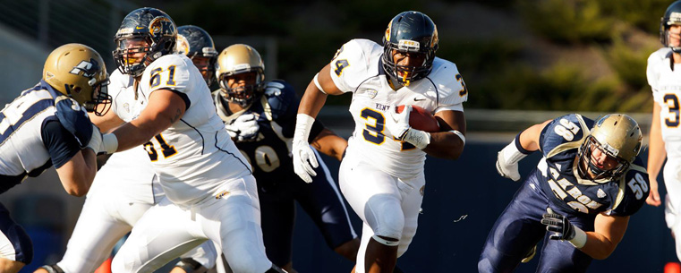 <p>A Kent State running back runs between Akron defenders for a gain.</p>