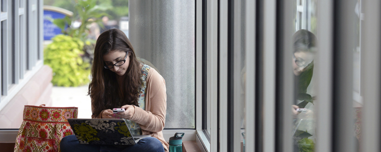 A Kent State student texts a friend while studying in the Roe Green Center lobby.