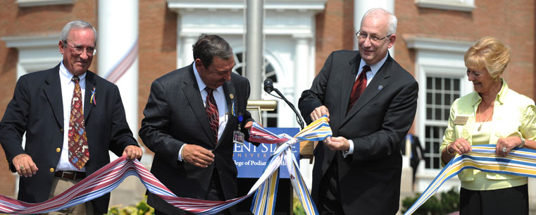 Dr. Stephen Berlin, former chair of the board of the Ohio College of Podiatric Medicine, Dr. Thomas Melillo, CEO of the College of Podiatric Medicine, Dr. Lester Lefton, President of Kent State University and Jacqueline Woods, Chairperson of the Kent State board of trustees, tie a ribbon signifying the joining of Kent State University and the Ohio College of Podiatric Medicine.