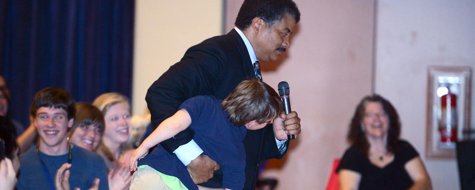 Neil deGrasse Tyson carries a young fan from the audience to the stage to ask the final question of the night.