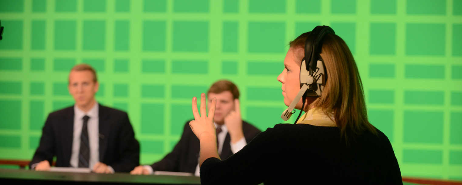 A TV2 floor director gives a signal to the on-air news team before the start of the 5:30 p.m. broadcast.