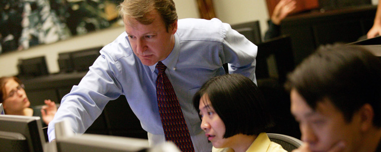 A professor assists undergraduate students on the Olga A. Mural Financial Engineering Trading Floor, located in Kent State's College of Business, which was recently voted a Best Business School by The Princeton Review.