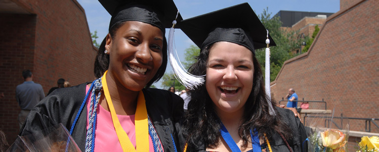 Two graduates pose for photos near the MAC Center following morning commencement ceremonies.