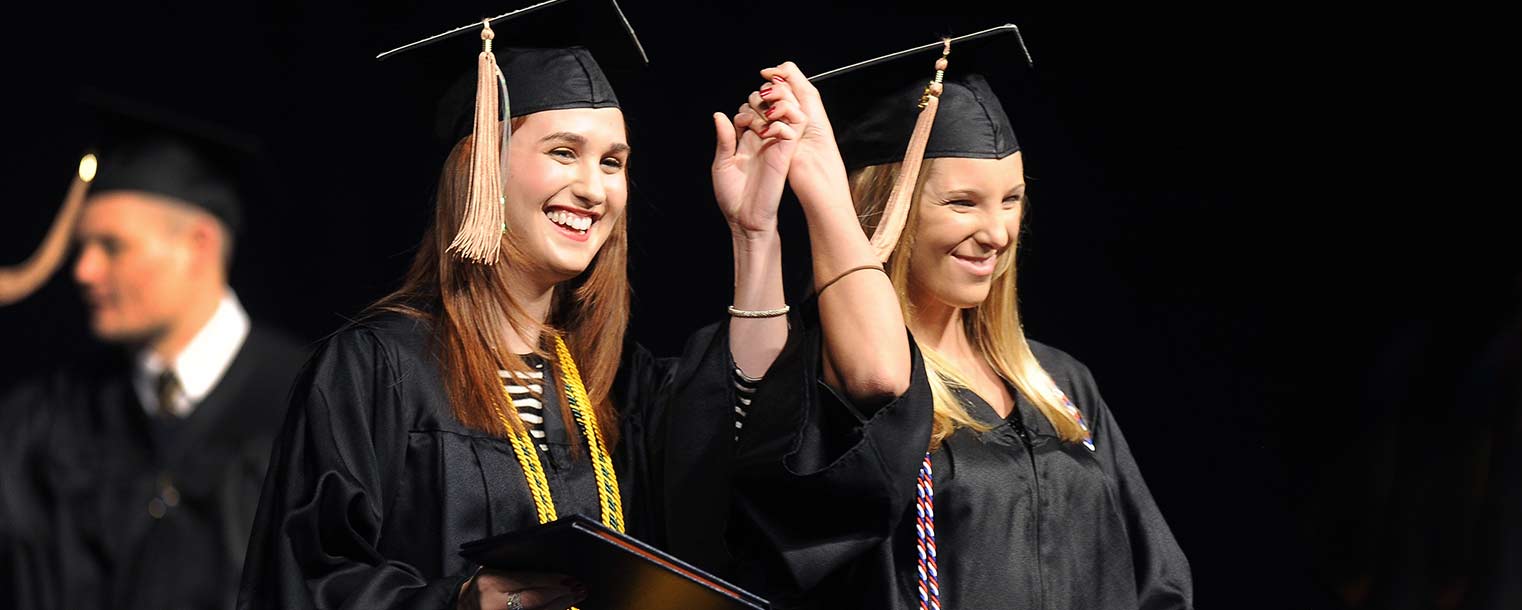 Two friends hold hands while walking across the stage after receiving their diplomas from Kent State in the Memorial Athletic and Convocation Center on Dec. 14.