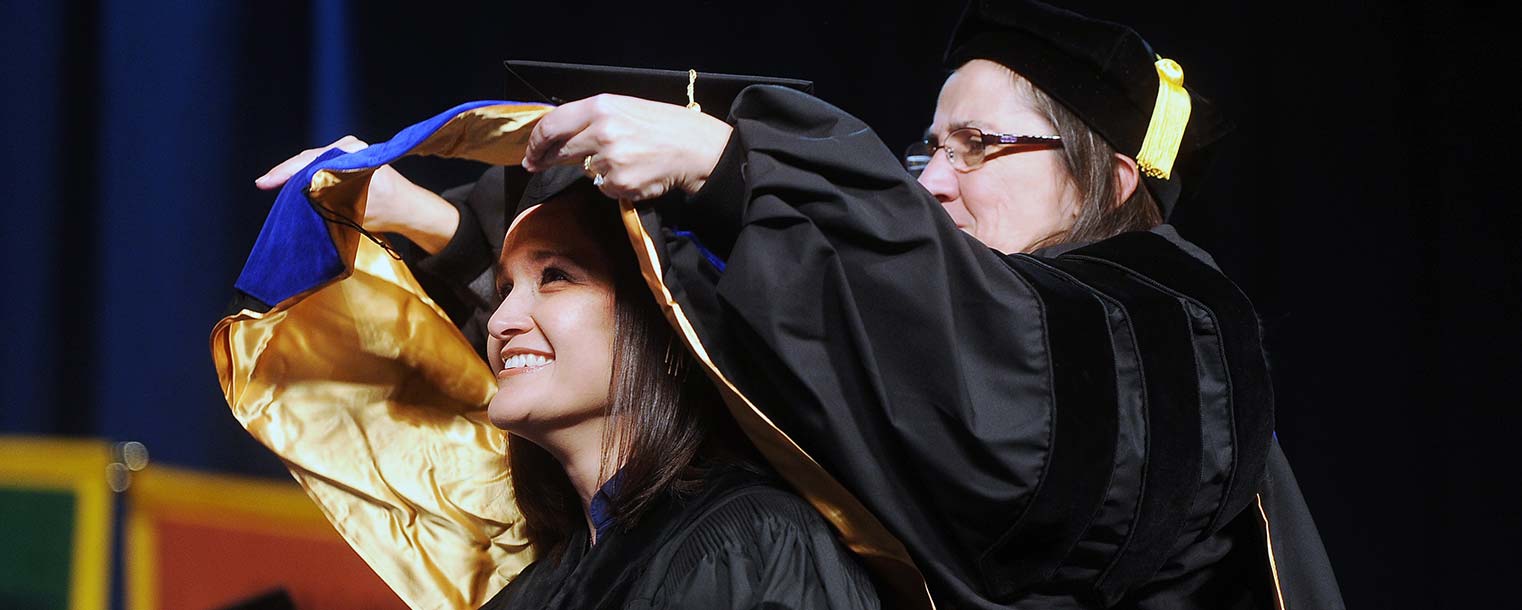 A graduate is hooded by her advisor during the conferral of doctorate degrees.