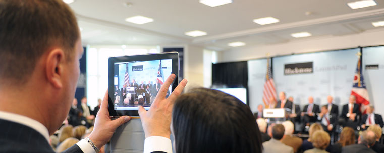 An attendee of the announcement captures the event on an iPad. The announcement involves Kent State University and three other Northeast Ohio colleges and universities.