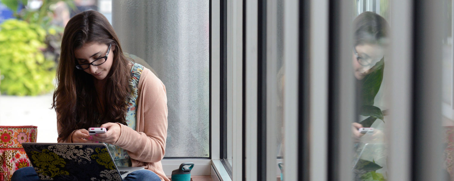 Kent State student texts a friend while studying in the Roe Green Center lobby.