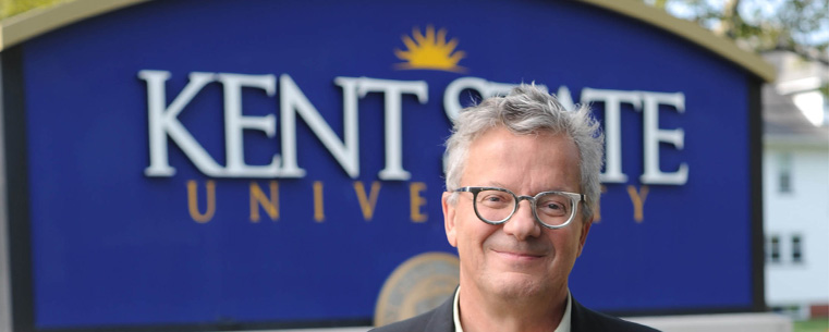 Mark Mothersbaugh, a founding member of the band Devo and music composer for television and movies, poses near the Kent State sign outside of Franklin Hall.