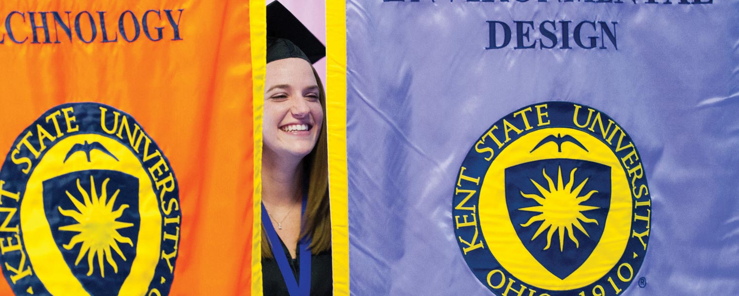 <p>A graduating senior spots family in the Memorial Athletic and Convocation Center as she passes between two banners during a recent Kent State Commencement ceremony.</p>