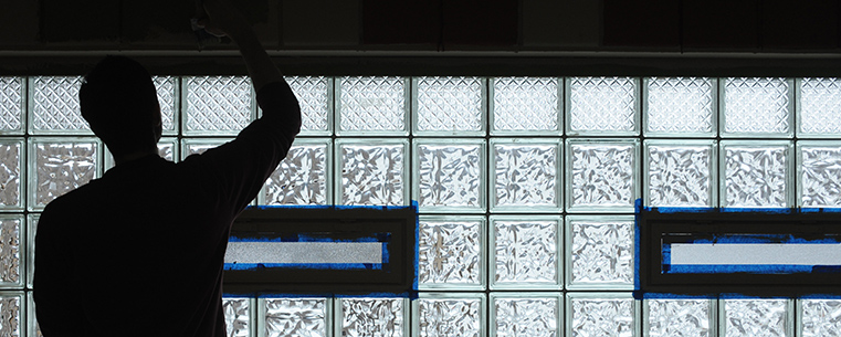 A Kent State student paints near a glass block window at the King Kennedy Community Center in Ravenna, Ohio.