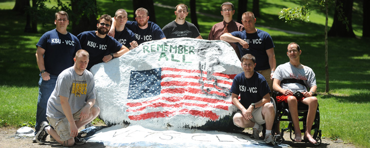 A group of veterans gather around the front campus rock after painting it in honor of current and former military personnel.