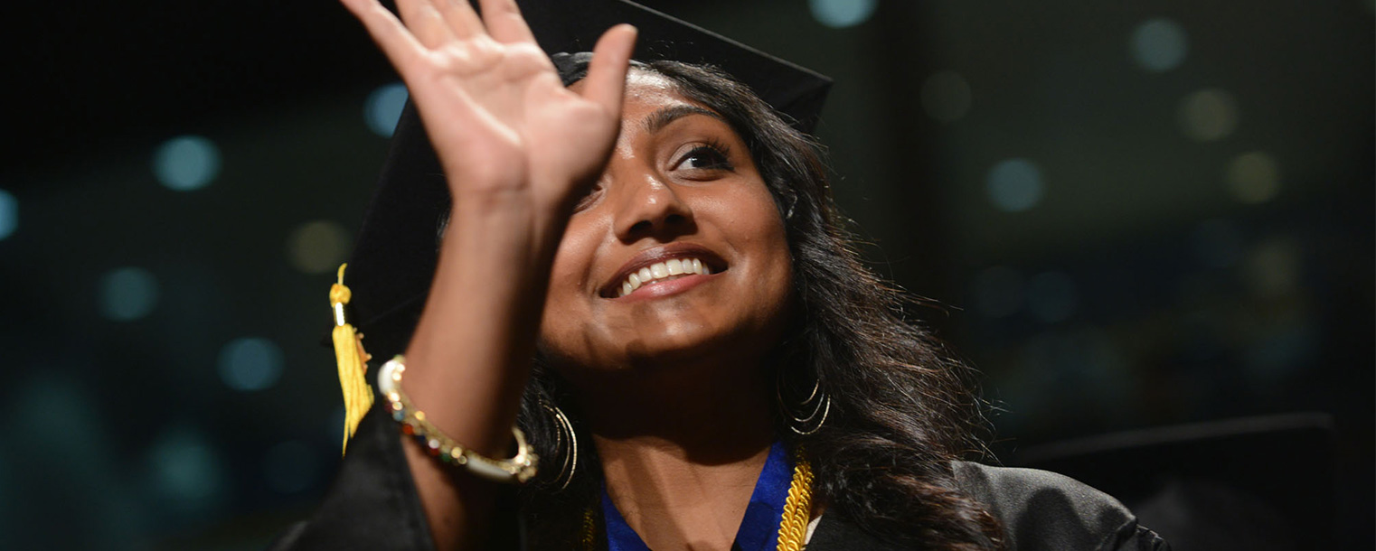 A summer 2013 graduate waves to her family while walking into the MAC Center for Kent State's commencement ceremonies.