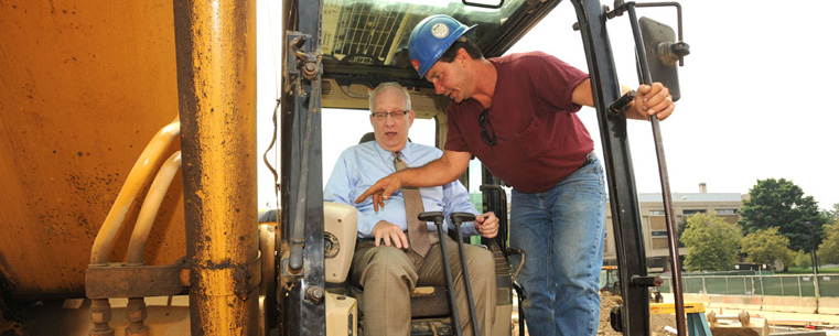 A worker from Cavanaugh Building Co. shows Kent State University President Lester A. Lefton how to work the controls on an excavator.