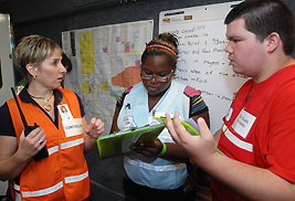 Nurse Kelly Englehart, a volunteer controller, assists two Upward Bound students during a mock disease outbreak held in collaboration with the Kent State College of Public Health.